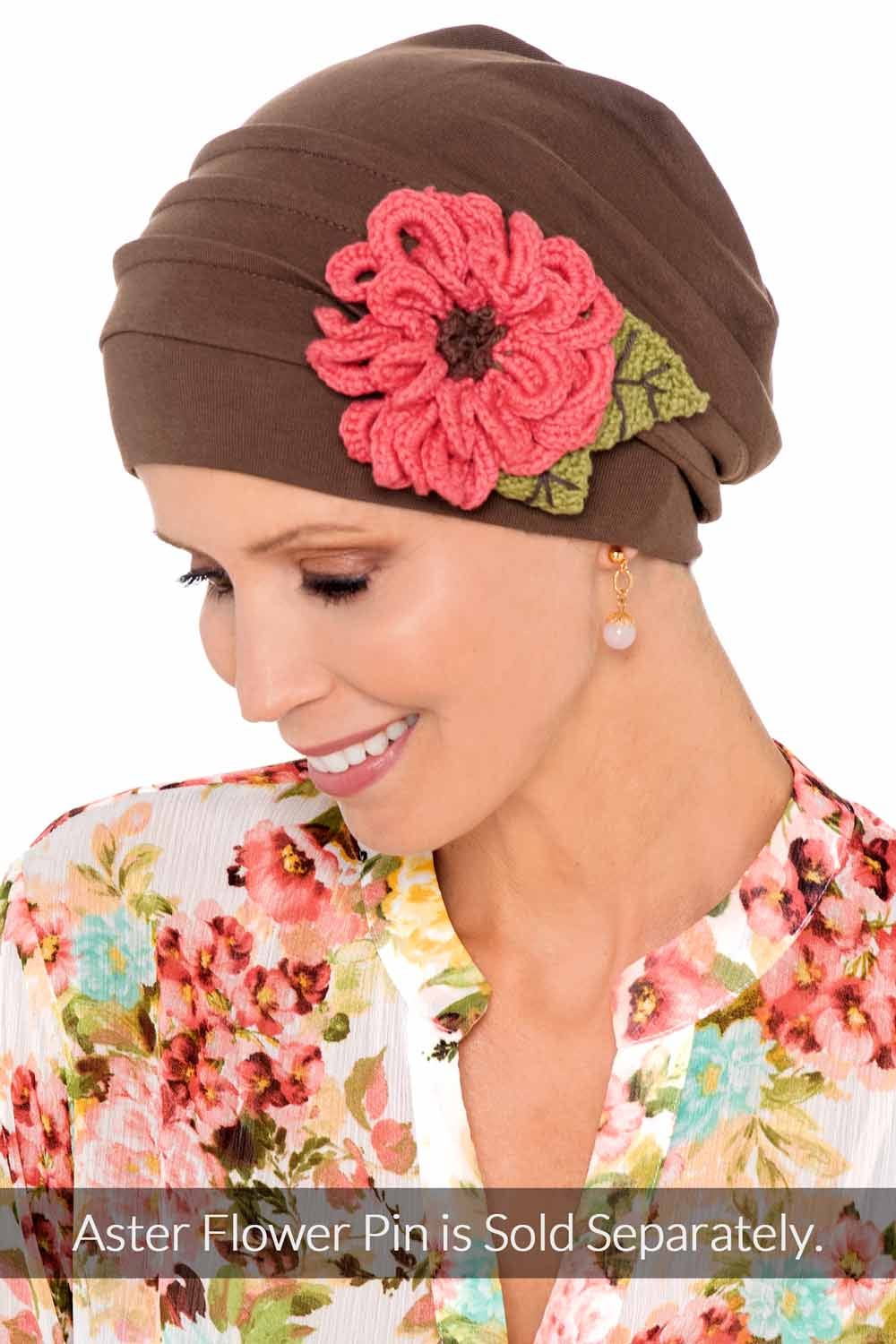 Smiling woman wearing brown snood style chemo hat with embroidered flower on the side