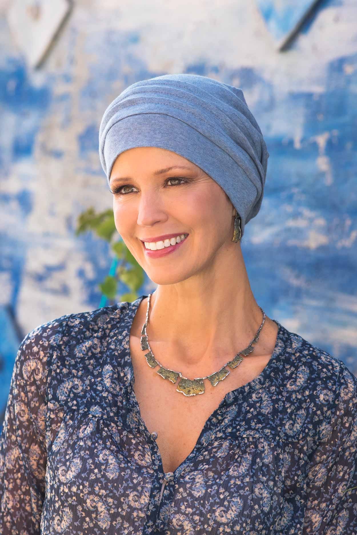 Woman outdoors by blue background wearing light denim blue colored snood hat